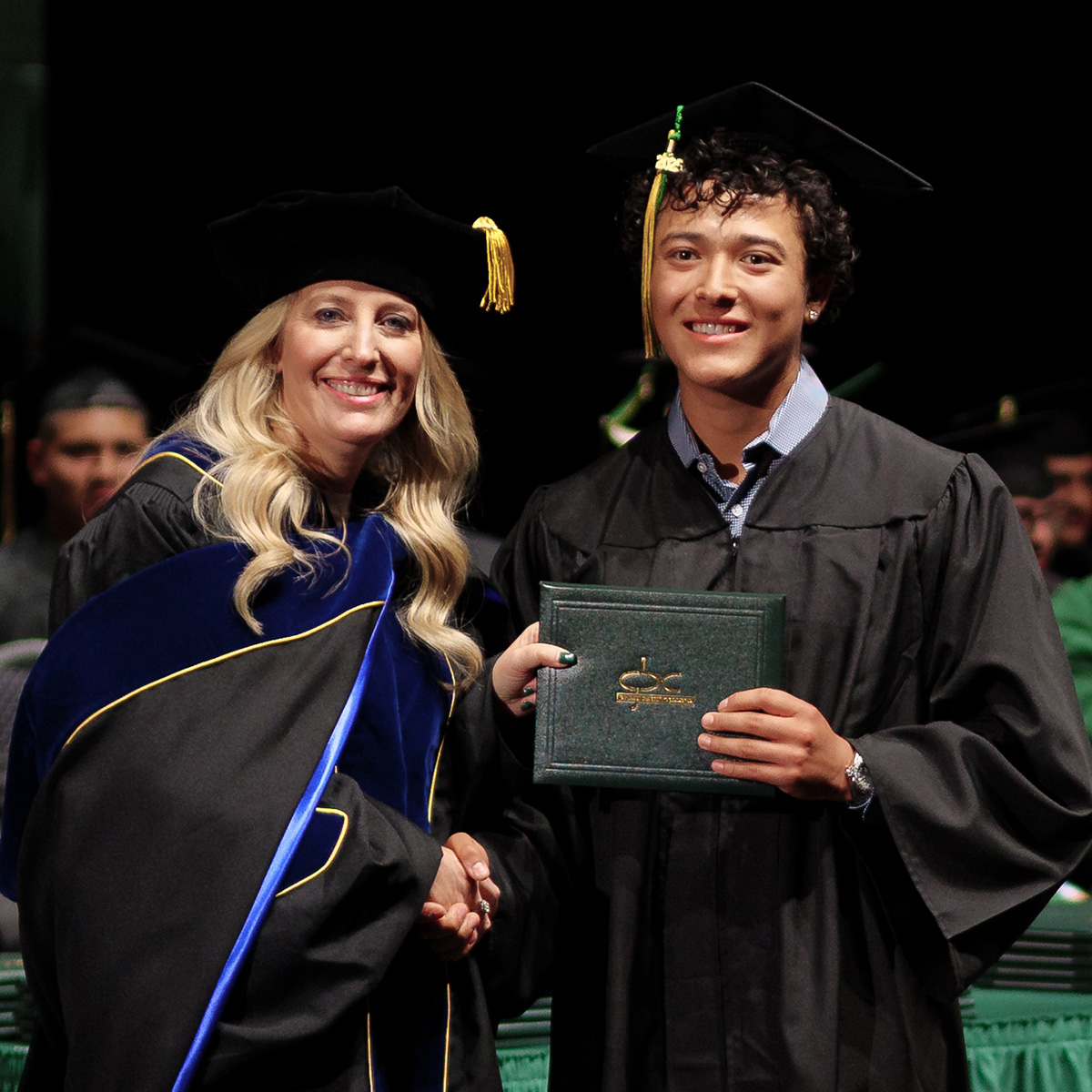 GBC President Amber Donnelli shakes hands with graduating student on stage.